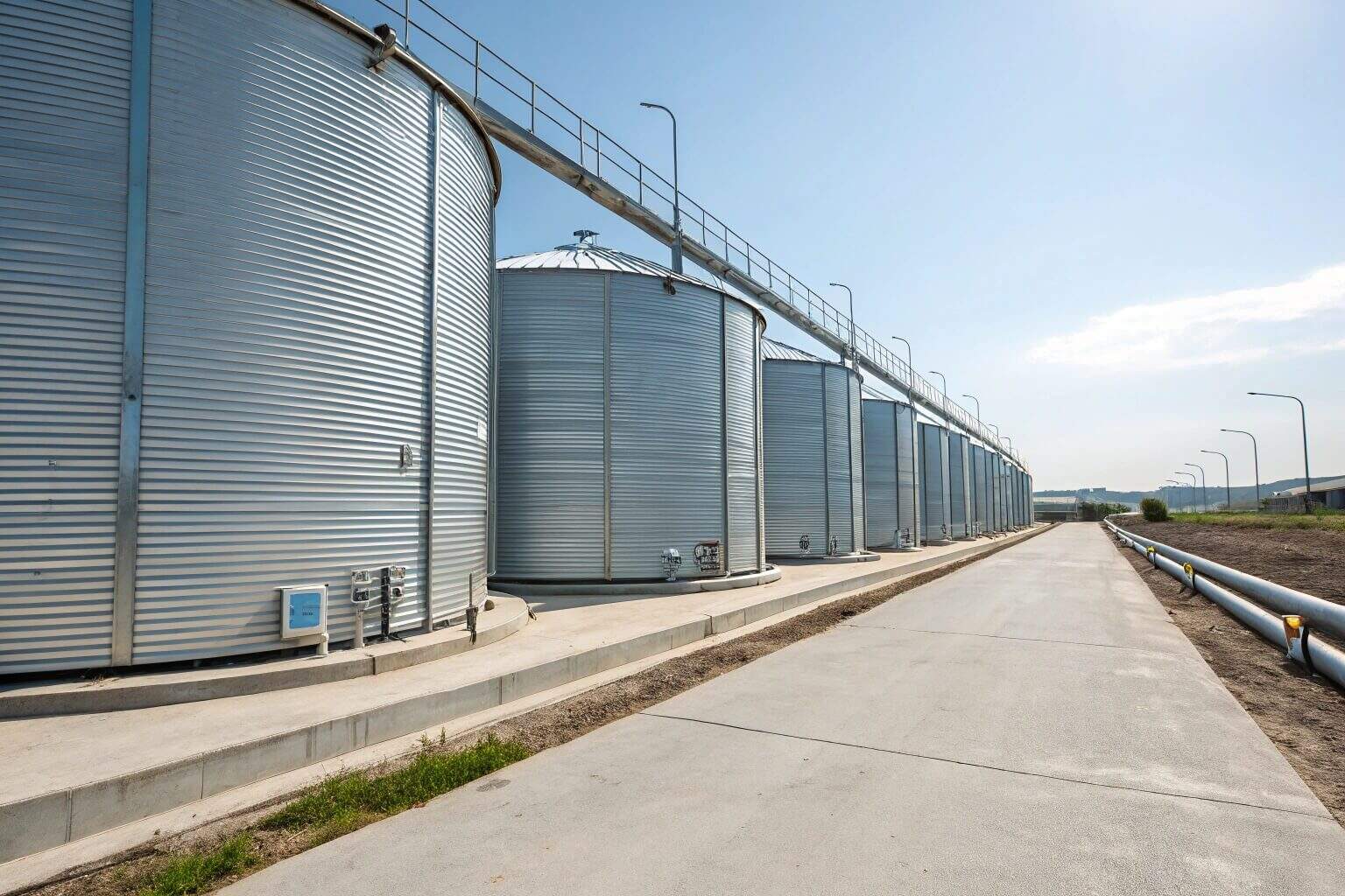 A wide-angle commercial photograph of a row of massive corrugated galvanized steel tanks in a modern fish farm, creating a powerful sense of scale and efficiency.