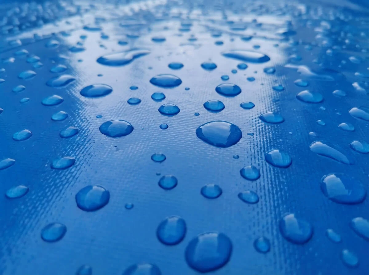 Macro texture of high-strength blue PVC knife coated tarpaulin showing glossy smooth surface.