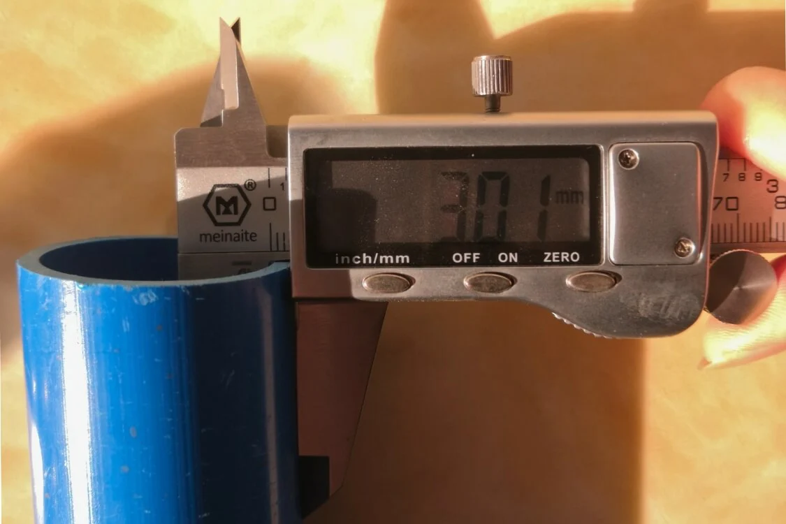 Digital caliper measuring the wall thickness of the industrial-grade white PVC pipe frame.